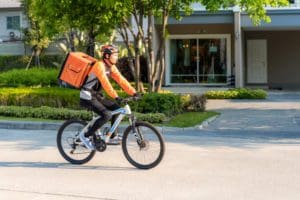 Asian,Man,Courier,On,Bicycle,Delivering,Food,In,Town,Streets